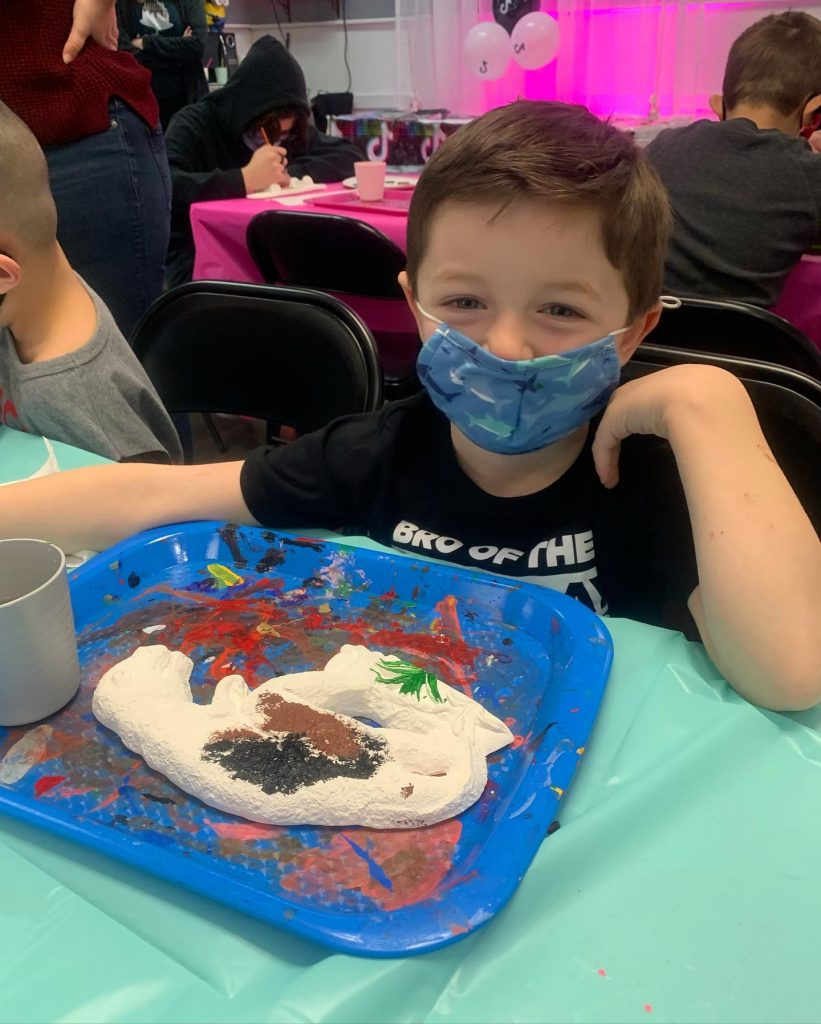 Happy boy in mask panting dinosaur plaster piece