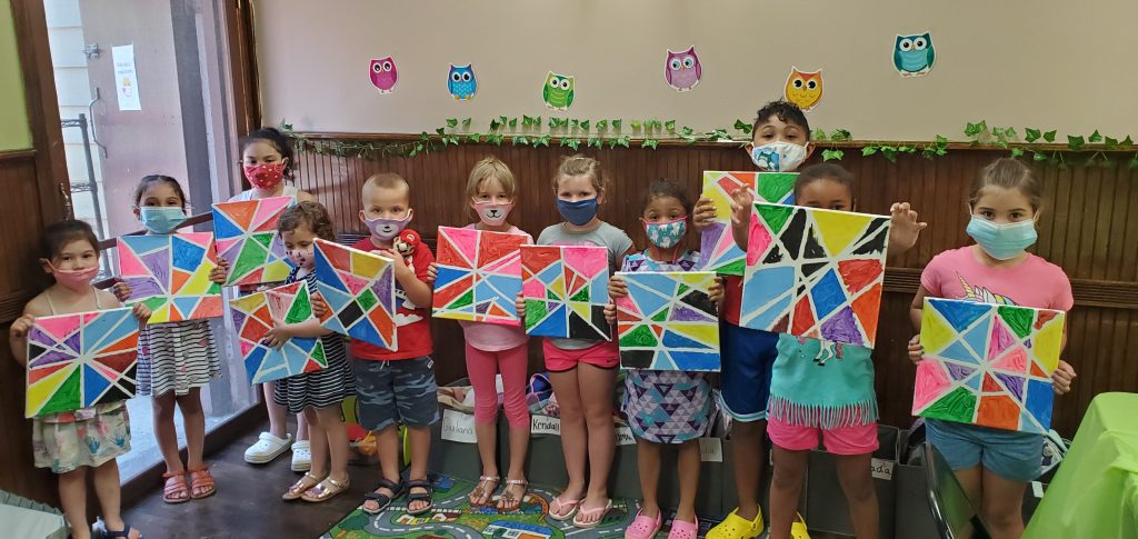 Children in masks showing mosaic themed canvas paintings