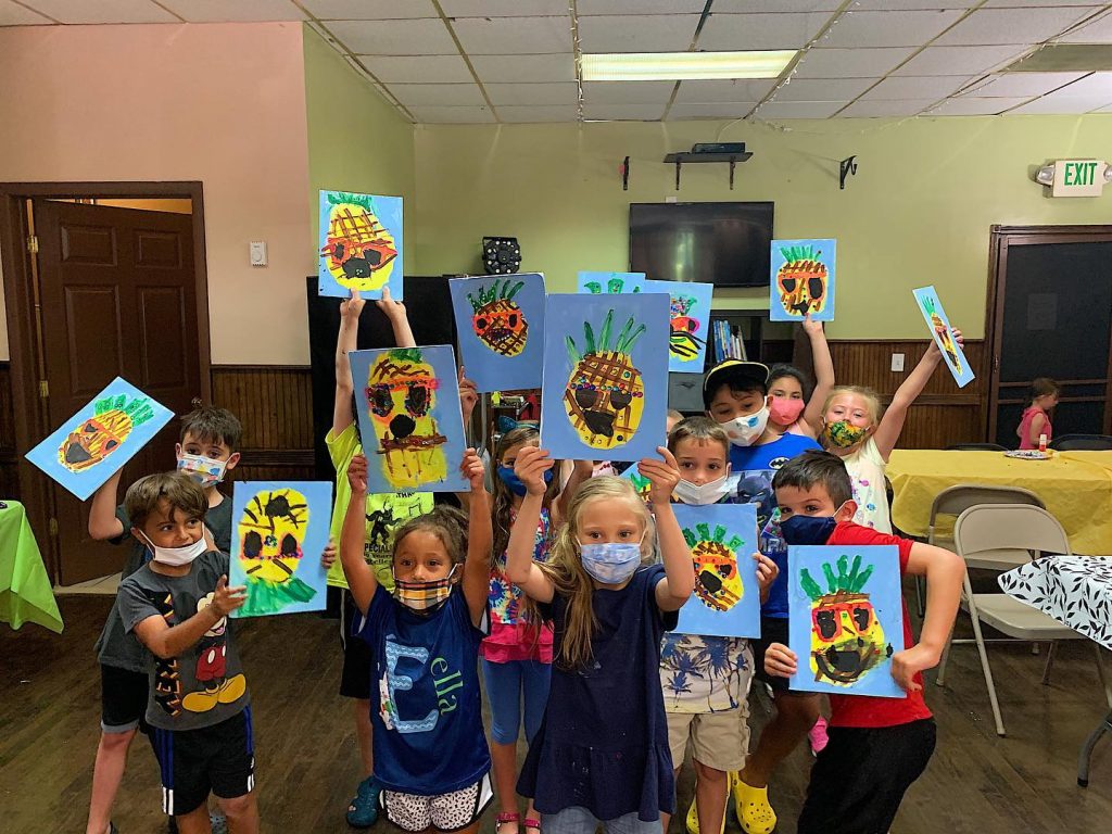 Kids in masks showing canvas painting of pineapple